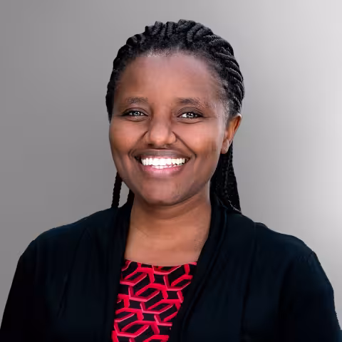 Gatwiri, wearing a black top and red patterned shirt, against a gray background.