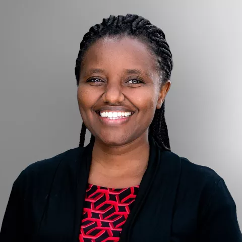 Gatwiri, wearing a black top and red patterned shirt, against a gray background.
