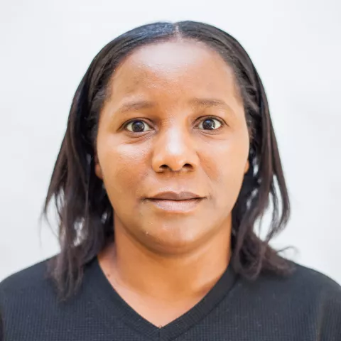 Getrude is wearing a black top. The background is plain white. 