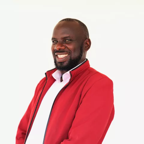 James wears a red jacket and white shirt. He is smiling at the camera, in front of a white background.