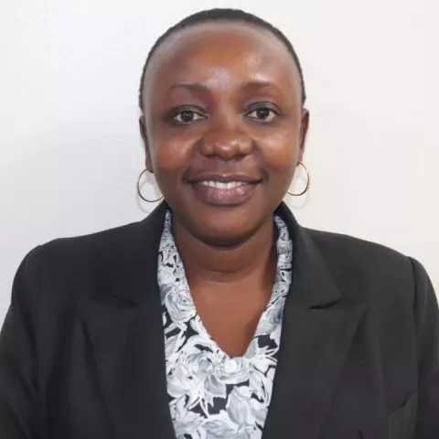 Jemma is in a black blazer and patterned blouse. She is standing against a plain white background.