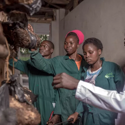 Three students in green overalls being guided by an instructor.
