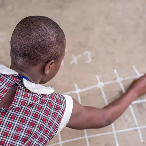 A schoolgirl does math sums with chalk on the ground of a classroom