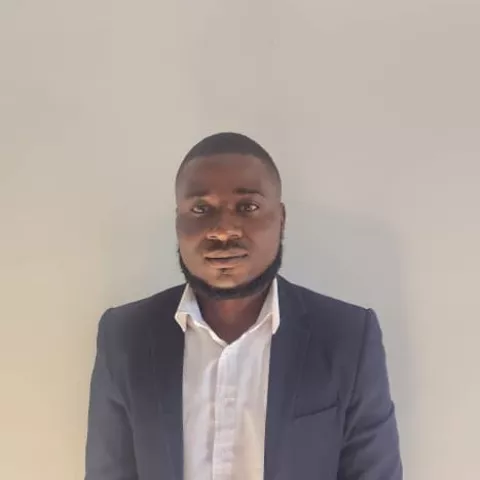 Kelly is wearing a grey suite over a white shirt. He is smiling lightly against a plain white background.