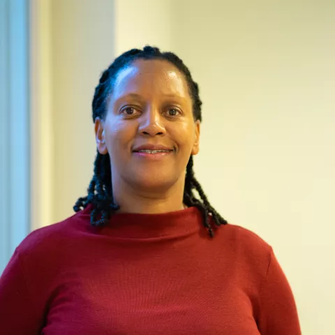 Kevina is wearing a red top and smiling. The background is a white wall.