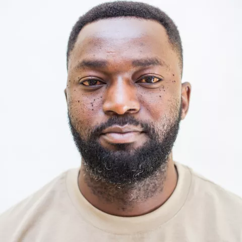 Kondwani is wearing a light brown shirt and smiles softly at the camera. The background is plain white.