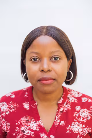 Mercy has hoop earrings and a straight expression. She is wearing a red floral blouse. The background is plain white.