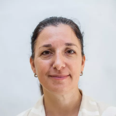 Miranda is wearing a striped white and beige shirt. She smiles against a white background.