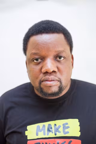 Mwimbu is wearing a black shirt that says "MAKE." The background is plain white.