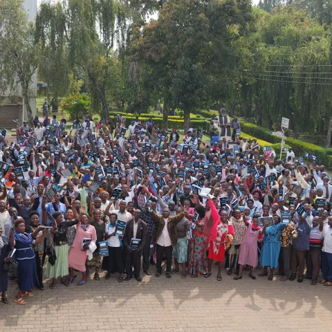 A large group of people stand outdoors raising their hands in celebration