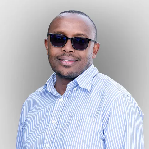 Peter, wearing sunglasses and a blue and white striped shirt stands against a light gray background.