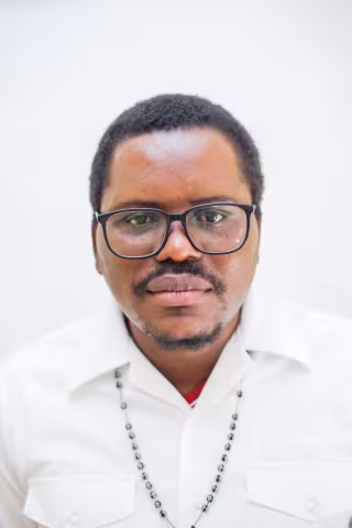 Pyopyo has black square glasses and is wearing a white shirt, looking directly at the camera with a neutral expression.