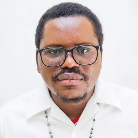 Pyopyo has black square glasses and is wearing a white shirt, looking directly at the camera with a neutral expression.