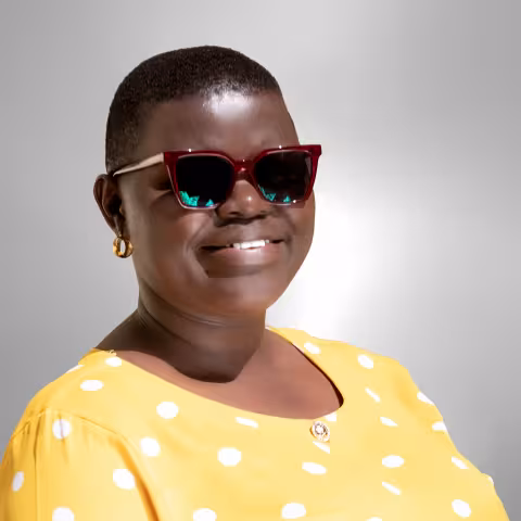  Rebecca is wearing dark red sunglasses and a bright yellow polka dot top. The background is a soft gray.