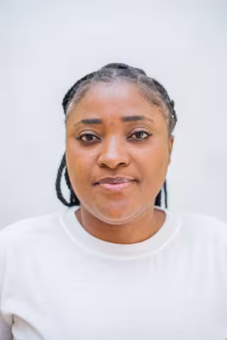Rhodah has a neutral expression. She is wearing a white shirt. The background is plain white. 