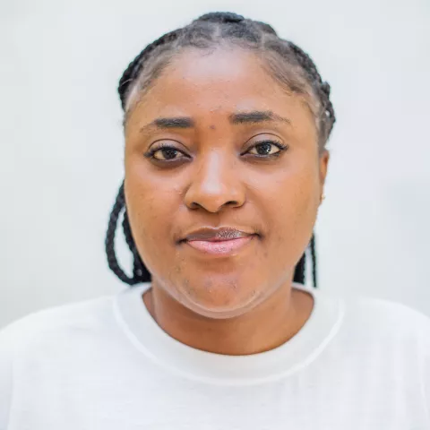 Rhodah has a neutral expression. She is wearing a white shirt. The background is plain white. 