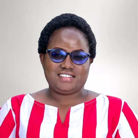 Risper is smiling while wearing blue glasses and a red and white striped shirt against a light gray background.