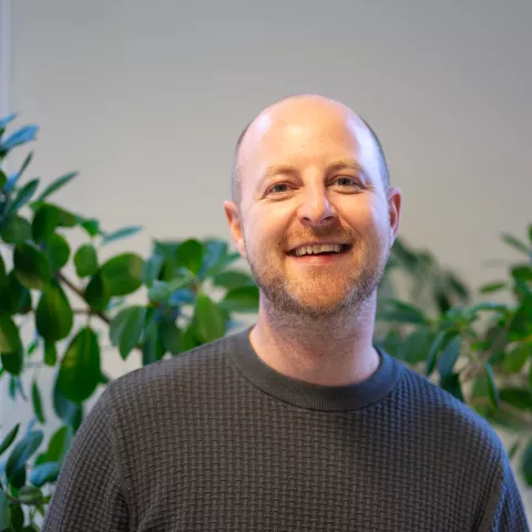 Rory is smiling at the camera, behind him a plant.