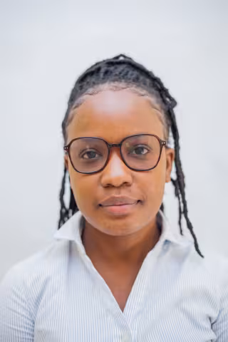 Saliya is wearing brown glasses and smiles lightly. She wears a white shirt against a plain white background.