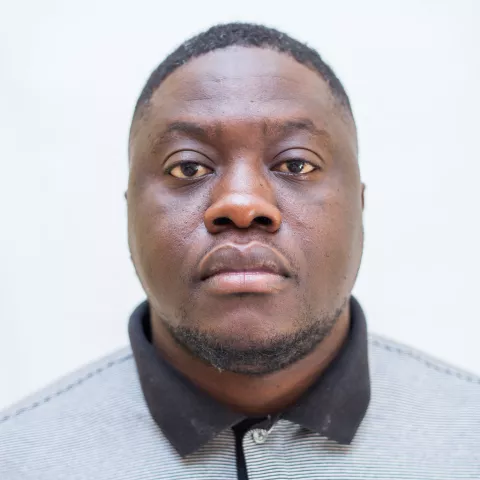 Vwambanji is wearing a polo shirt and looks directly into the camera. The background is plain white.