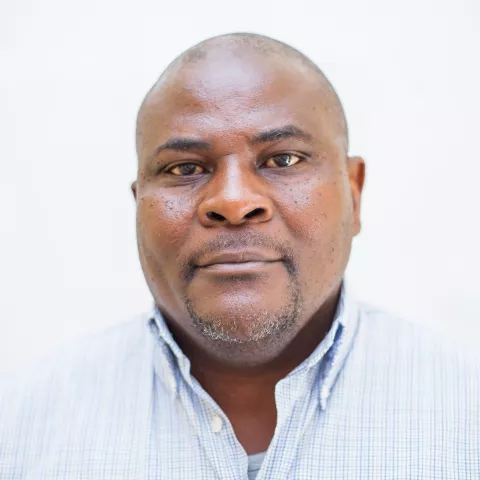 Walubita is wearing a blue checkered shirt. The background is plain white