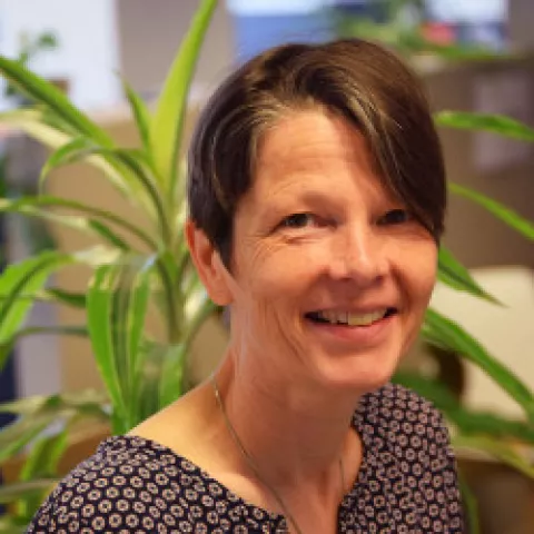 Kristine is standing in front of a plant, smiling