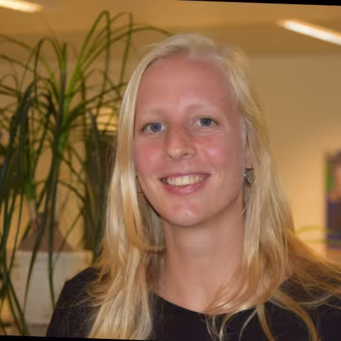 Sofie is wearing a black shirt and smiling. In the background there are plants.